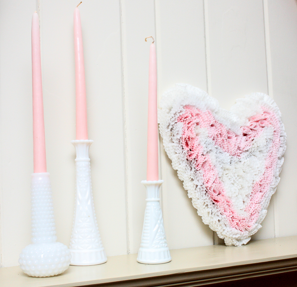 Three milk glass vases with pink candles and a cardboard heart decorated with pink and white cupcake liners