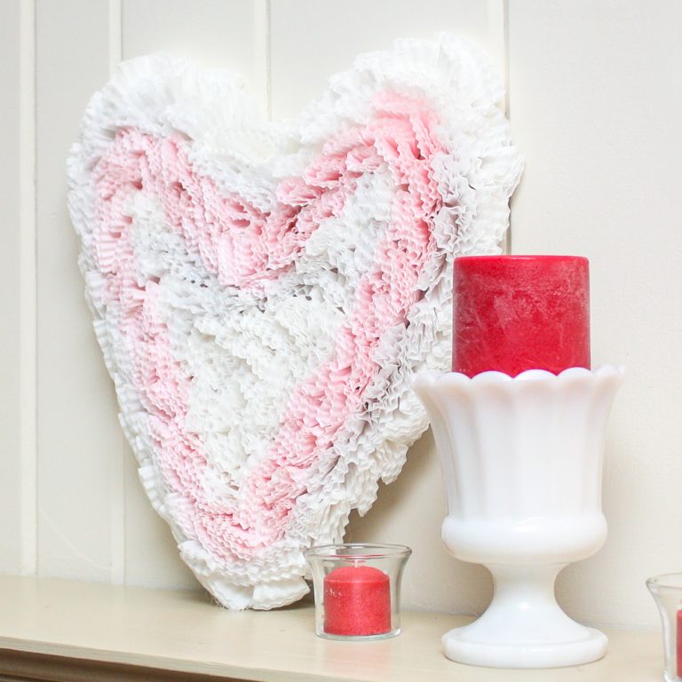 Handmade cupcake liner heart displayed with a milk glass compote with a dark pink candle and a clear votive with a matching votive candle