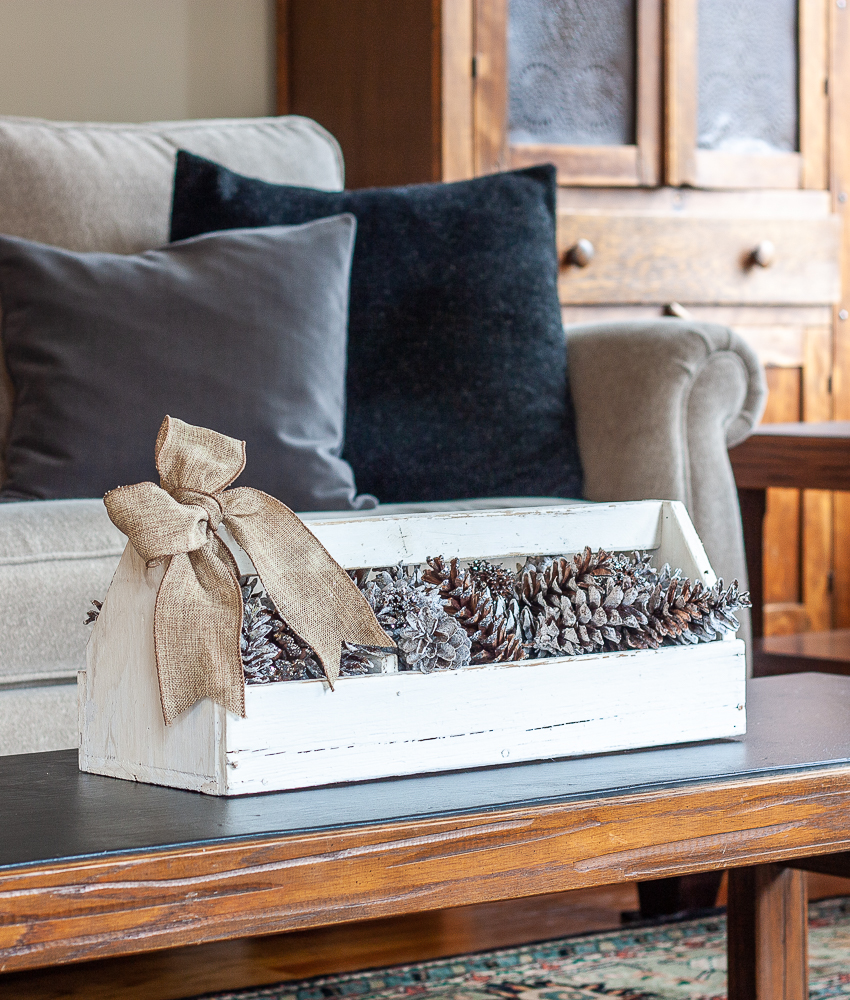 Vintage toolbox decorated for winter with glittered and snow-kissed pinecones and a burlap bow.