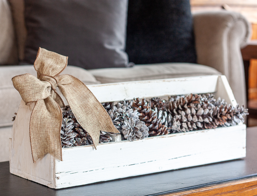 Vintage toolbox decorated for winter with glittered and snow-kissed pinecones and a burlap bow.