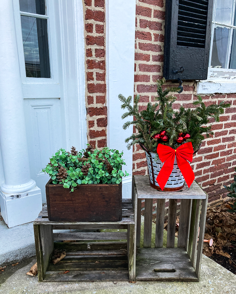 Vintage toolbox decorated with Eucalyptus and pinecones and olive bucket filled with Christmas greenery on crates.