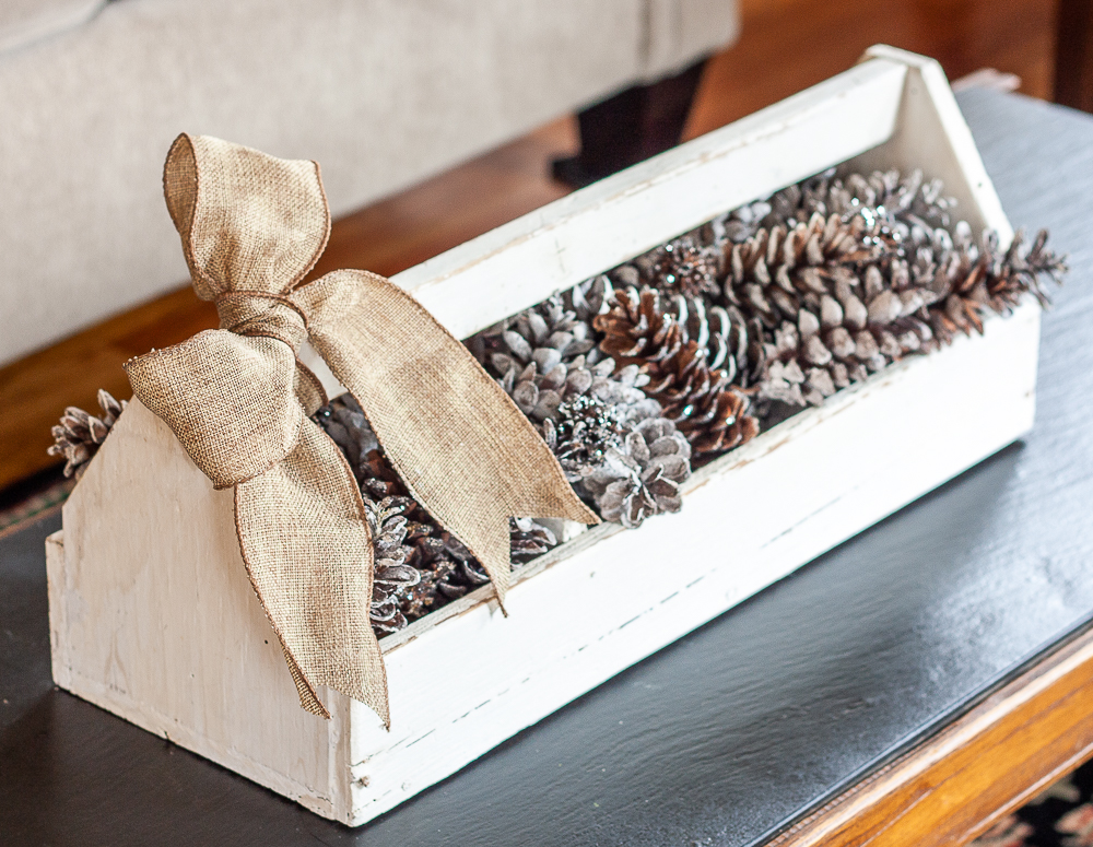 Vintage toolbox decorated for winter with glittered and snow-kissed pinecones and a burlap bow.