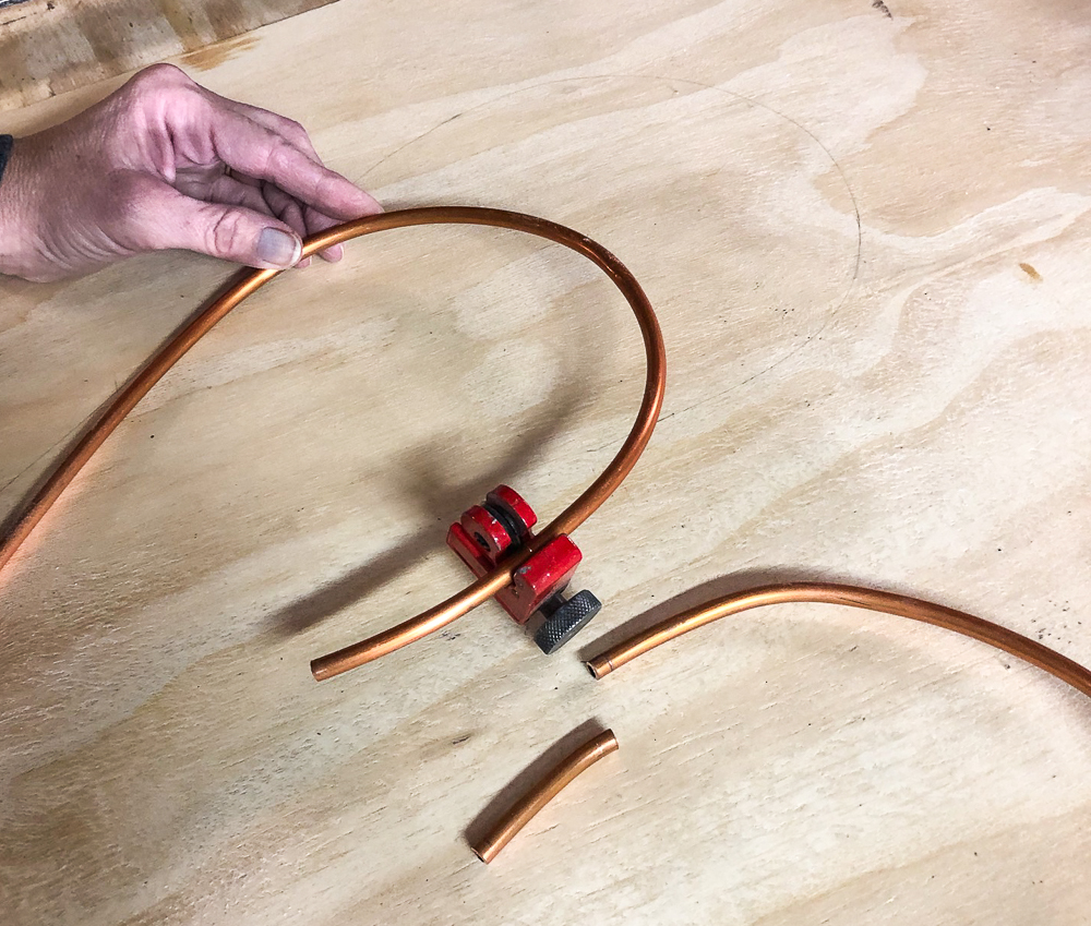 Cutting a copper water line pipe with a pipe cutter.
