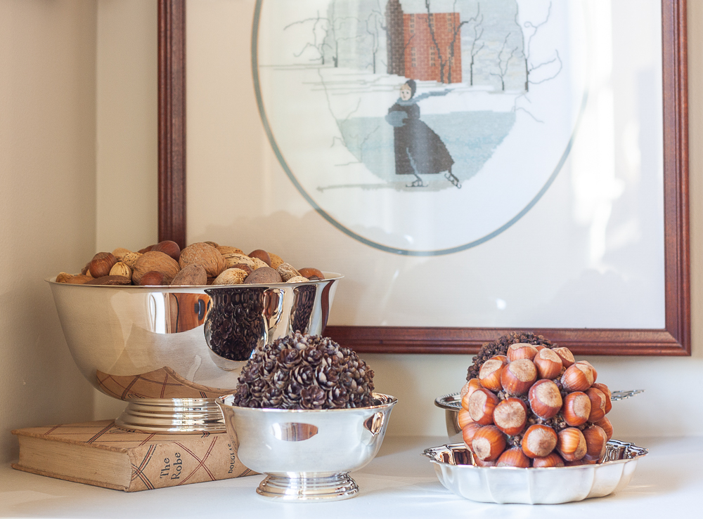 Mixed nuts in their shell in a silver bowl, balls crafted with hemlock cones, hazelnuts, and cloves in silver bowls