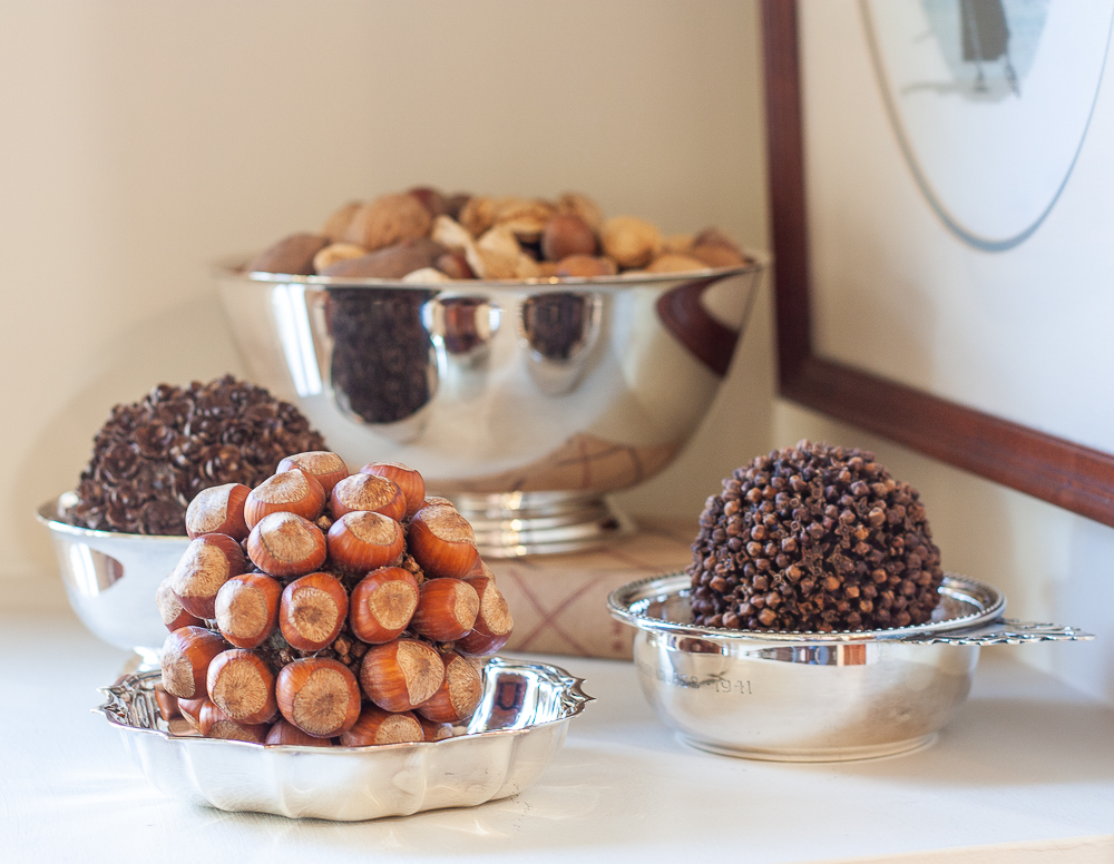 Mixed nuts in their shell in a silver bowl, balls crafted with hemlock cones, hazelnuts, and cloves in silver bowls