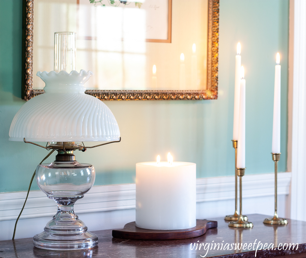 White candles used for winter decor along with an antique oil lamp with a white shade