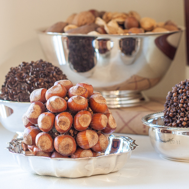 Mixed nuts in their shell in a silver bowl, balls crafted with hemlock cones, hazelnuts, and cloves in silver bowls