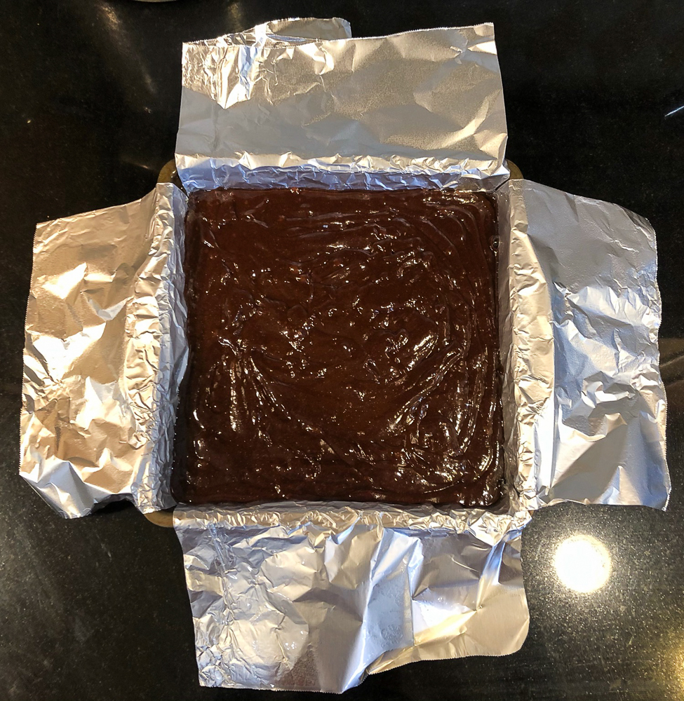 Brownie batter in a square pan lined with aluminum foil