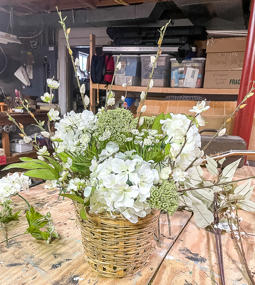 3 hydrangea blooms, pussy willow stems, flowering apple stems, and queen anne's lace looking blooms in a woven basket