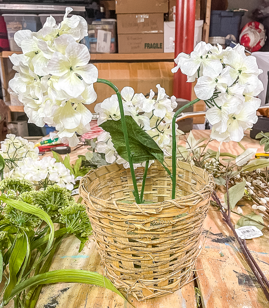 Three faux hydrangea blooms in a woven basket