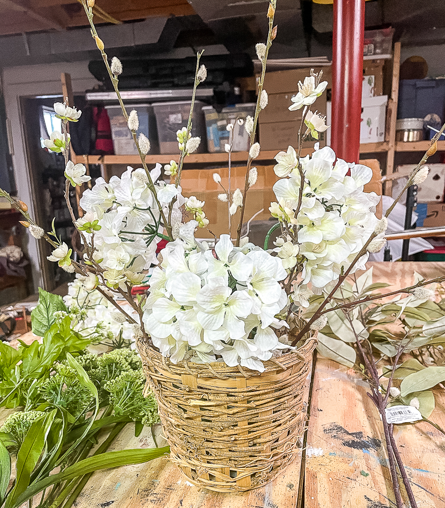 3 hydrangea blooms, pussy willow stems, and flowering apple stems in a woven basket