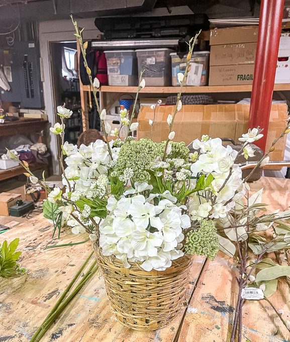 3 hydrangea blooms, pussy willow stems, flowering apple stems, and queen anne's lace looking blooms in a woven basket