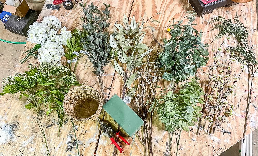 Faux flower stems and greenery on a wood worktop ready to be made into a spring centerpiece