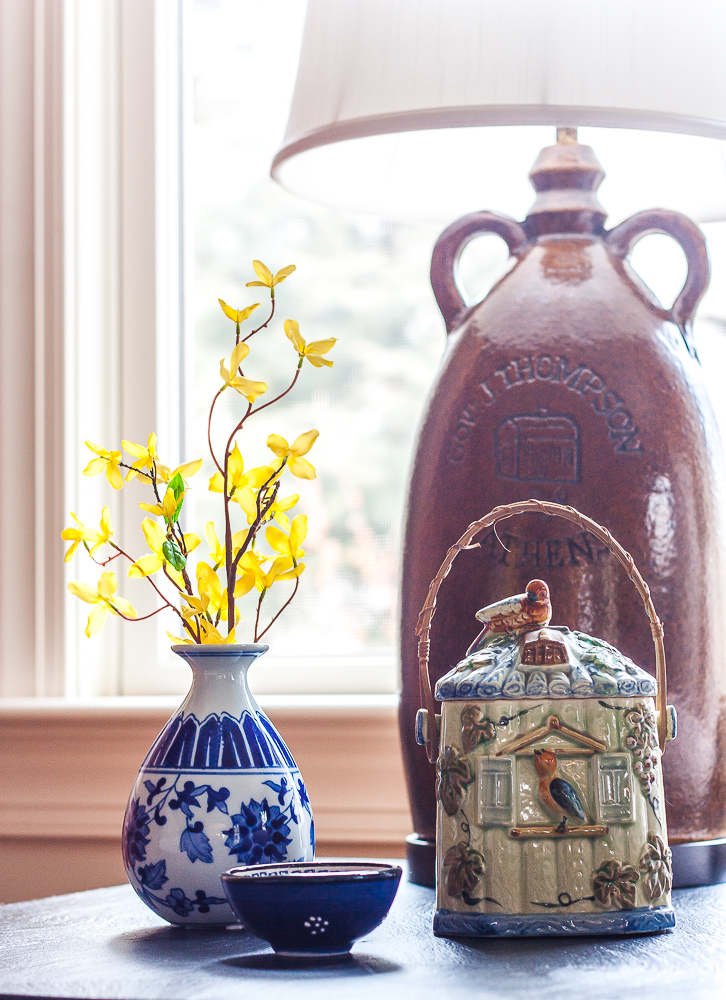Spring vignette with a blue and white vase filled with Forsythia, a small blue bowl, and a vintage pottery piece that looks like a birdhouse.