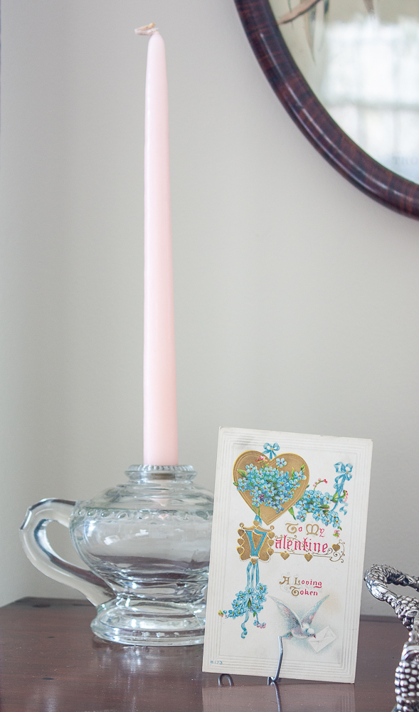 Vintage oil lamp used as a candle holder with a pink candle and an early 1900s Valentine's Day postcard