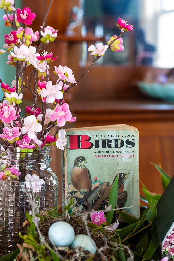 Pink faux florals in a vintage, clear, embossed Mason jar with a bird nest, and 1949 Birds A Golden Nature Guide