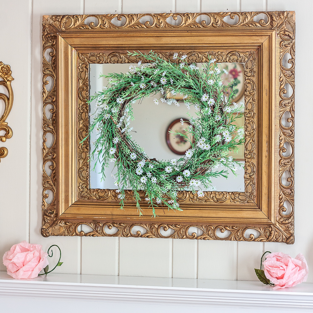 Spring wreath with greenery and tiny daisies hanging on an antique gold mirror