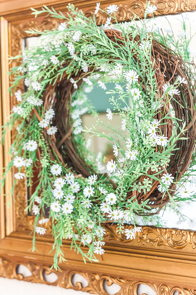 Spring wreath with greenery and tiny daisies hanging on an antique gold mirror