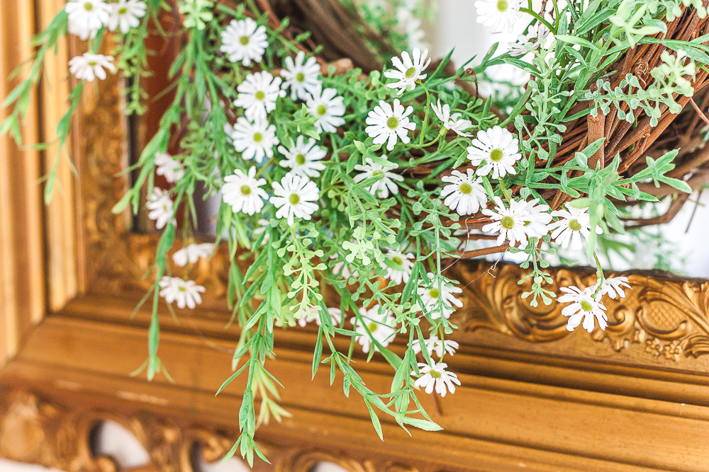 Spring wreath with greenery and tiny daisies hanging on an antique gold mirror