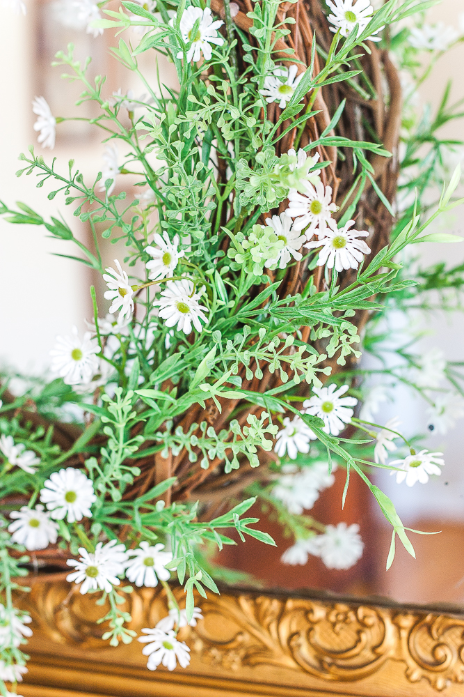 Spring wreath with greenery and tiny daisies hanging on an antique mirror