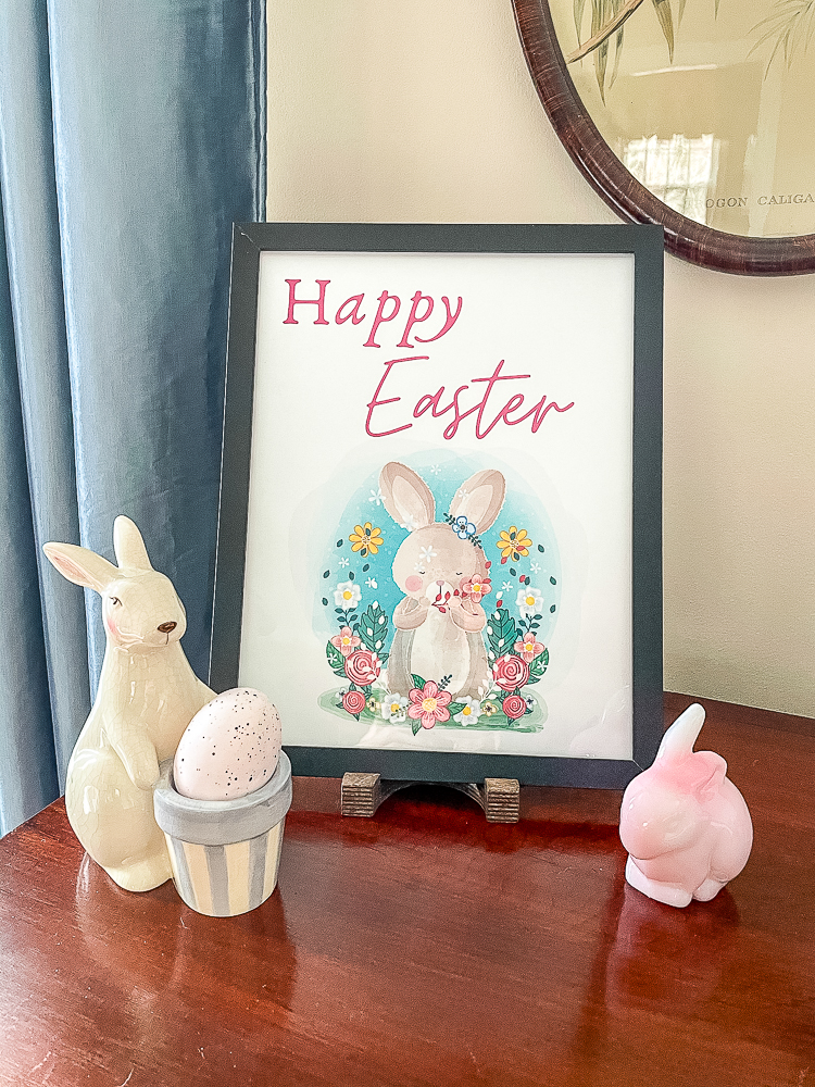 Happy Easter printable in a black frame with a pink Fenton rabbit and a ceramic rabbit holding a basket that holds an egg