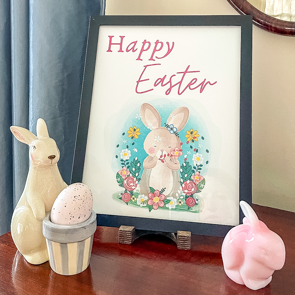 Happy Easter printable in a black frame with a pink Fenton rabbit and a cream rabbit holding a basket that holds an egg