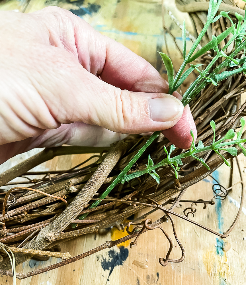 Adding a sprig of faux greenery to a grapevine wreath