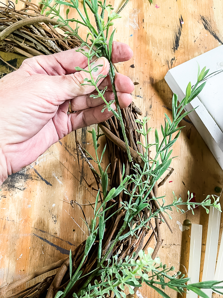 Adding a sprig of faux greenery to a grapevine wreath