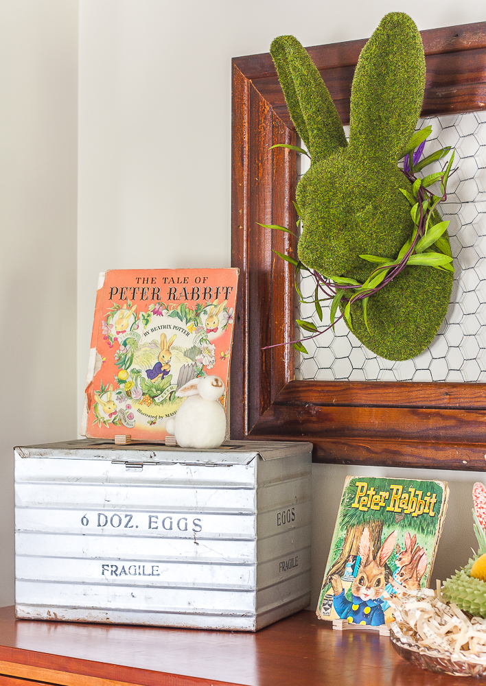 Moss covered rabbit hanging on a frame with chicken wire, 1942 and 1961 Peter rabbit books, and an antique egg shipping crate