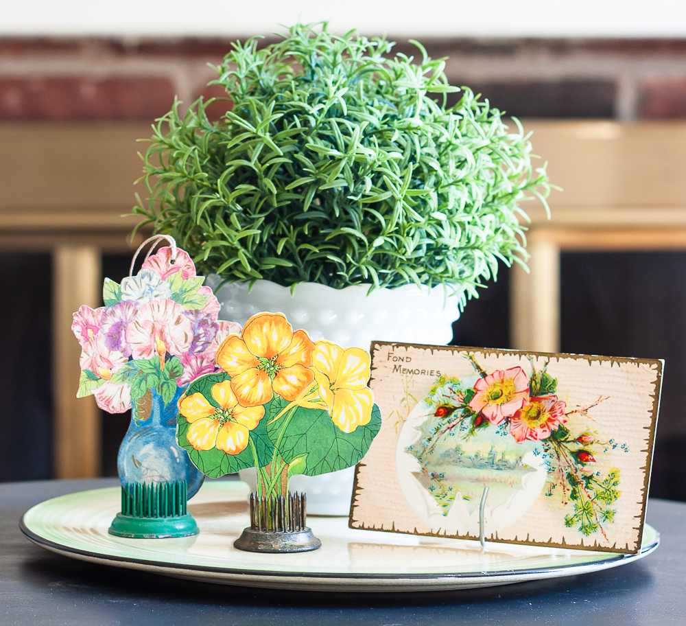 Spring vignette with a faux plant in a milk glass pot, vintage bridge tally cards, and a postcard from the early 1900s