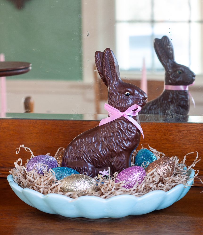 Faux chocolate rabbit in a blue dish with shredded paper and glittered eggs