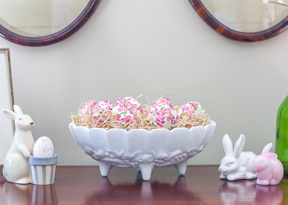 Decoupaged Easter eggs displayed in a milk glass fruit bowl with bunnies displayed on either side