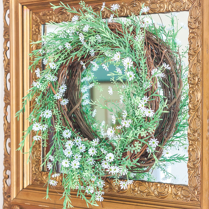 Spring wreath with greenery and tiny daisies hanging on an antique gold mirror