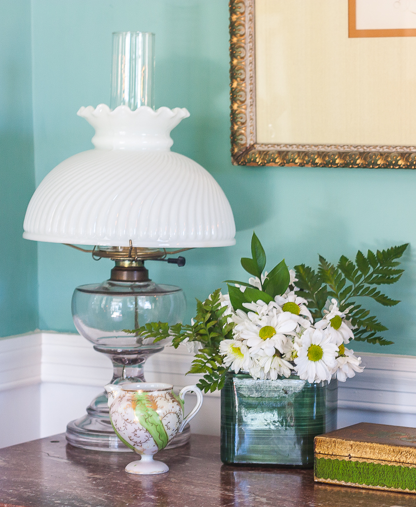 Antique lamp, antique green and gold pitcher, flower arrangement with daisies and ferns