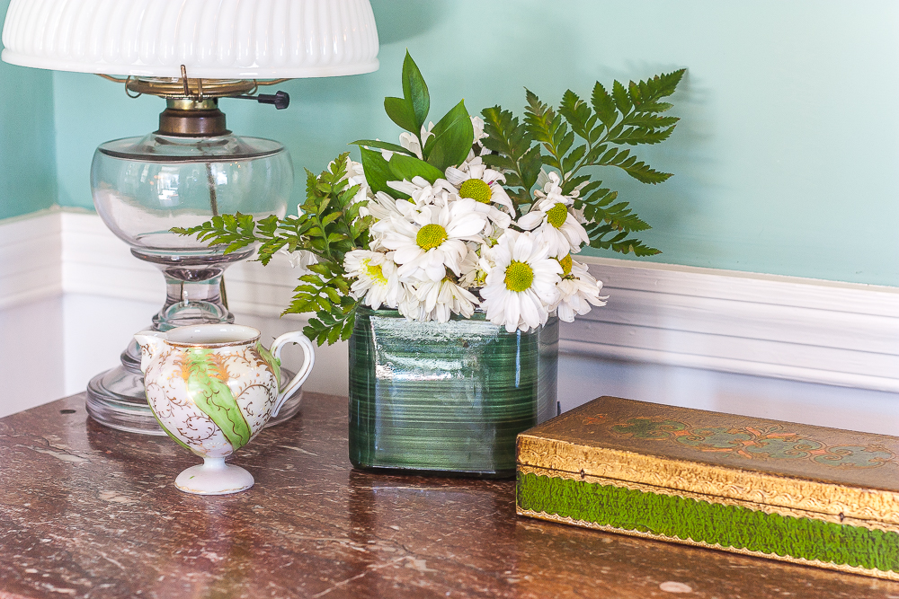 Antique lamp, antique green and gold pitcher, flower arrangement with daisies and ferns, and a vintage green and gold box