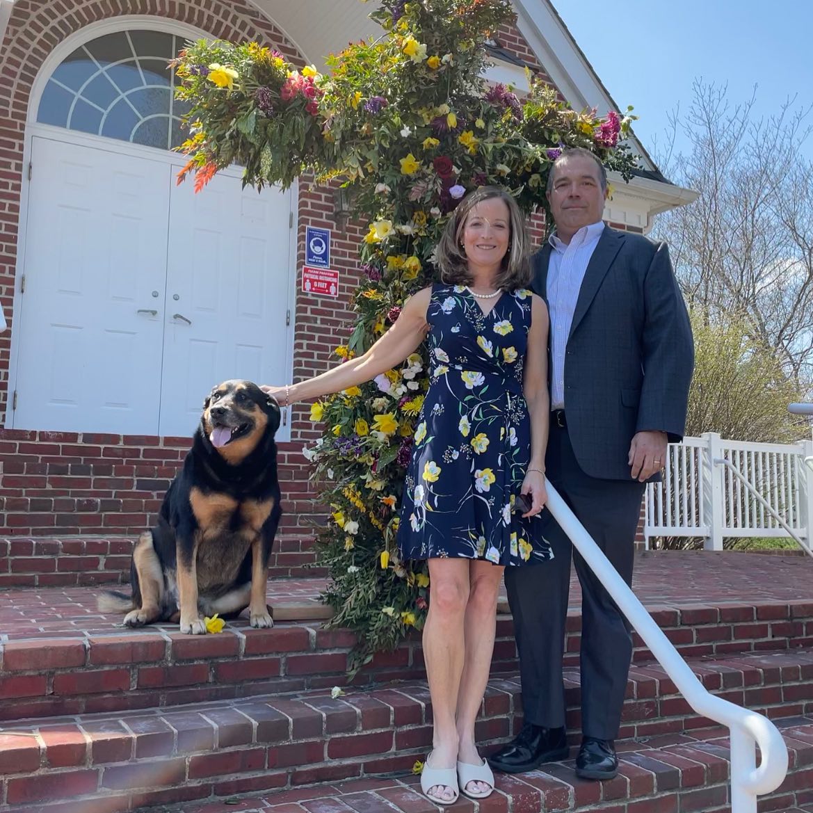 Couple and dog in front of a cross decorated with flowers on Easter Sunday