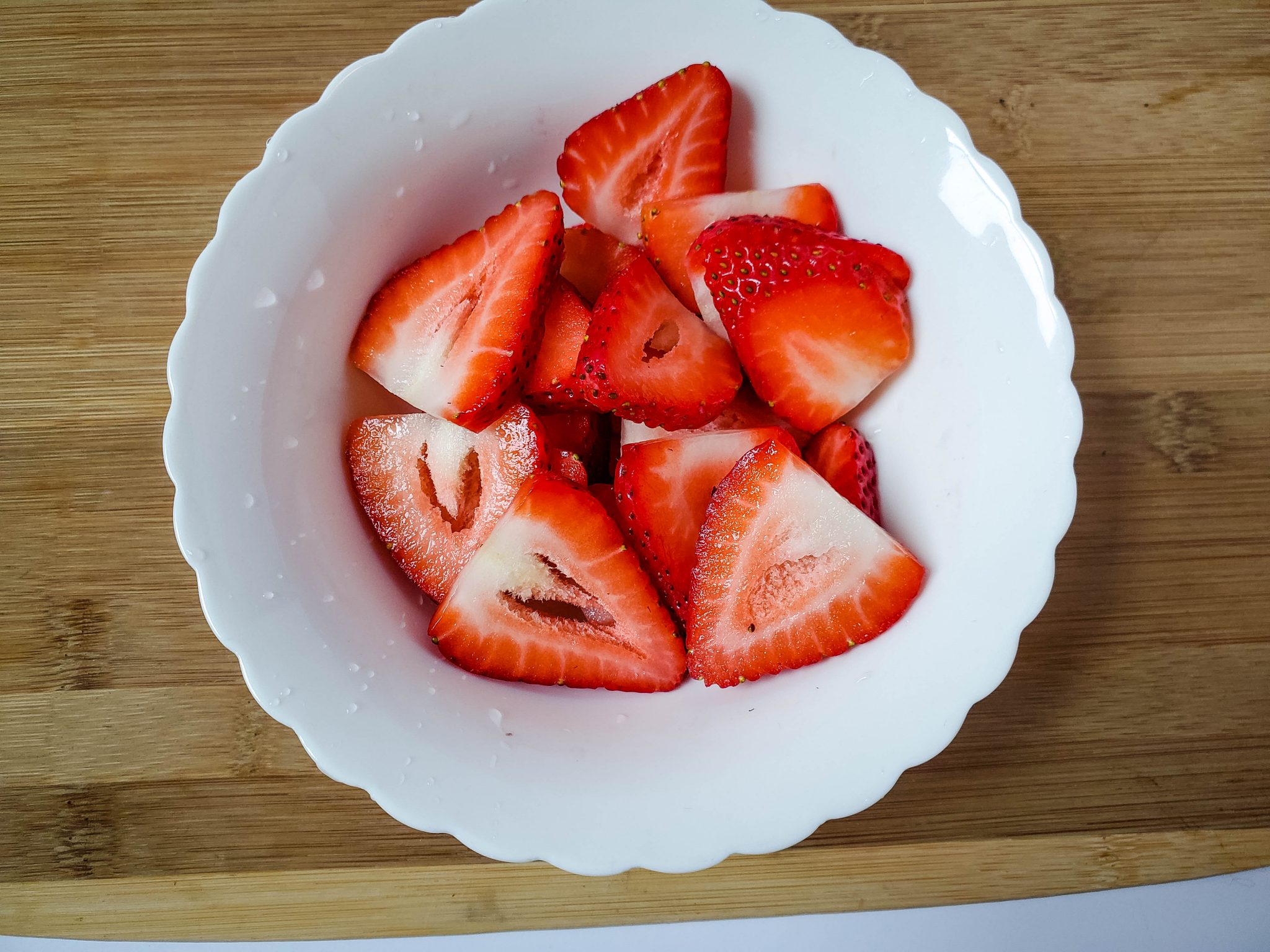 Slices of strawberries in a white bowl on a wood cutting board