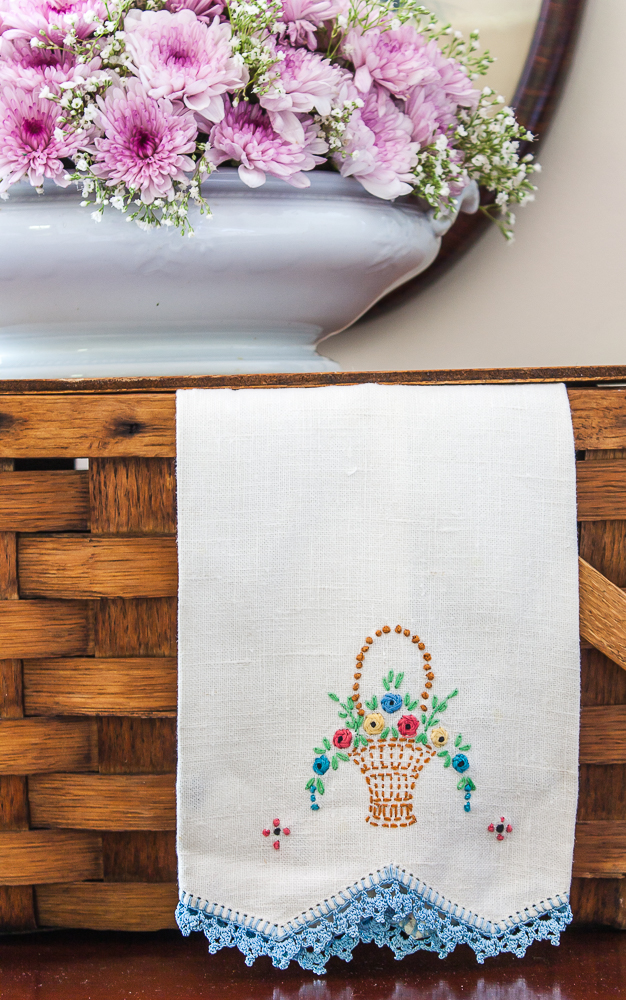 Vintage embroidered tea towel on a picnic basket with a floral arrangement in an antique Ironstone dish.