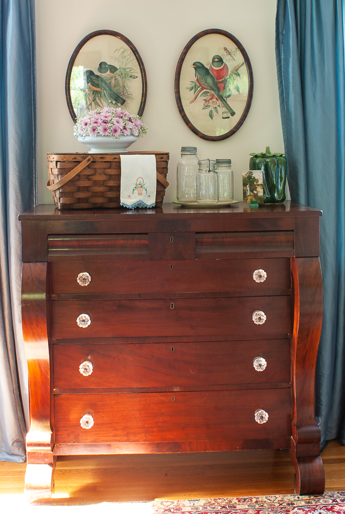 Antique chest of drawers decorated for summer with a picnic basket, flower arrangement, tea towel , Mason jars, a McCoy green pepper cookie jar, and an antique postcard.