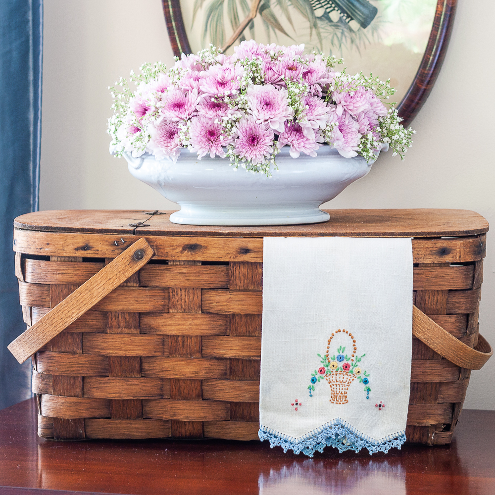 Vintage picnic basket with a floral arrangement, and vintage embroidered tea towel