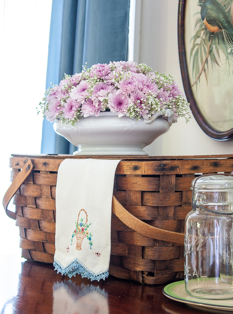 Vintage picnic basket with a floral arrangement in an antique Ironstone serving dish, vintage embroidered tea towel, and a Mason jar