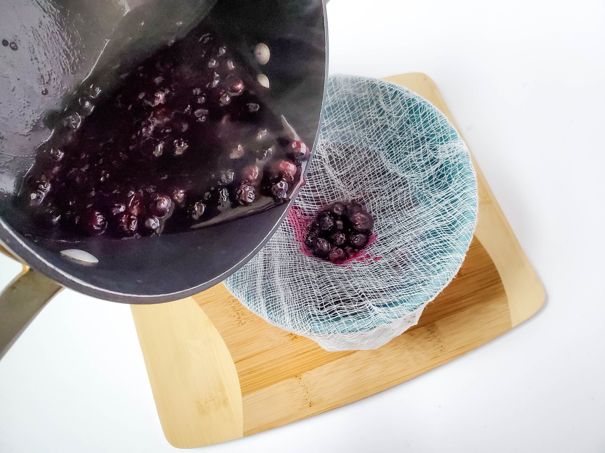 Straining blueberry juice over a bowl lined with cheesecloth