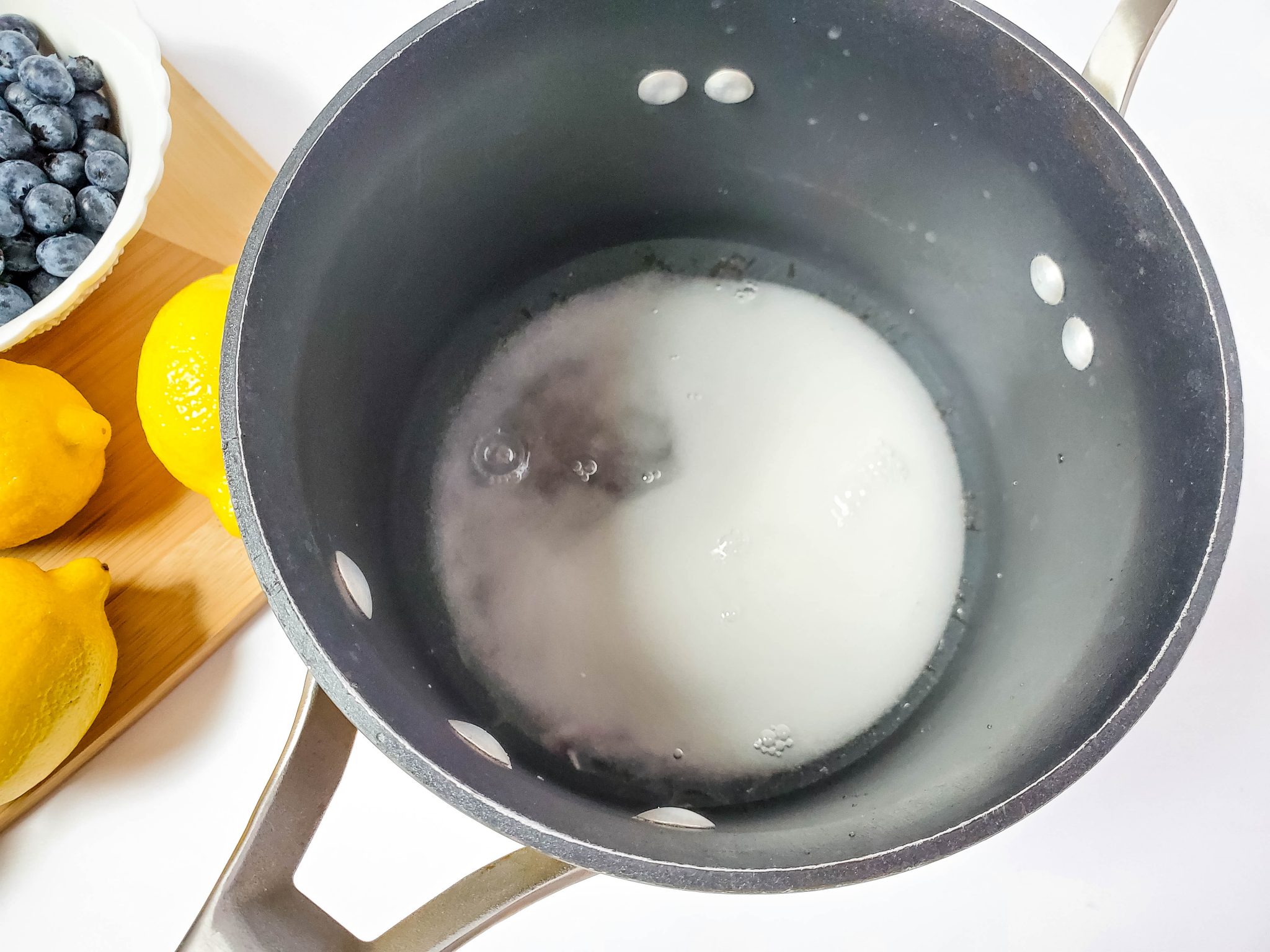 Melted sugar in a pan along with fresh blueberries and lemons to make homemade blueberry lemonade