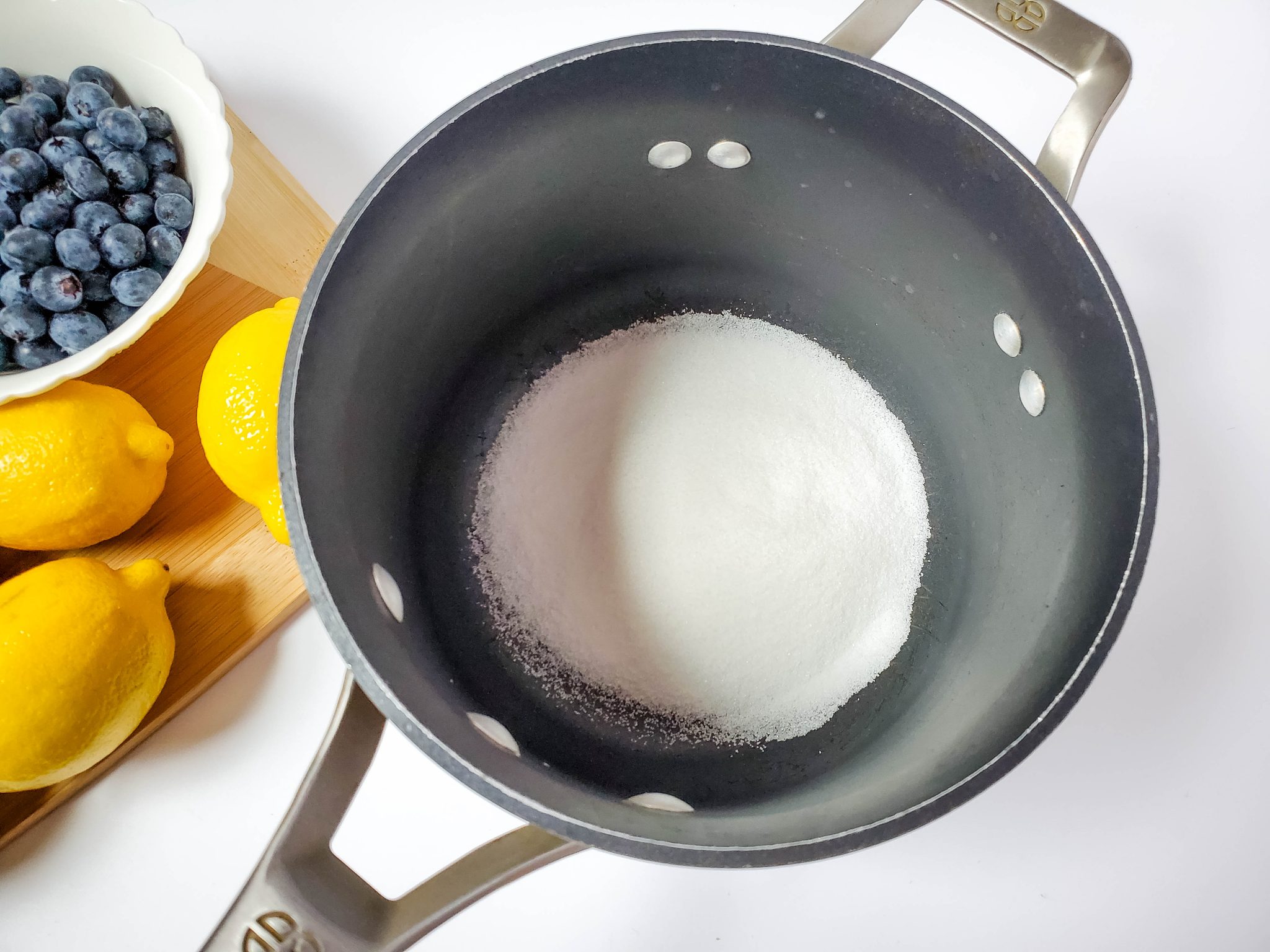 Sugar in a pan along with fresh blueberries and lemons to make homemade blueberry lemonade