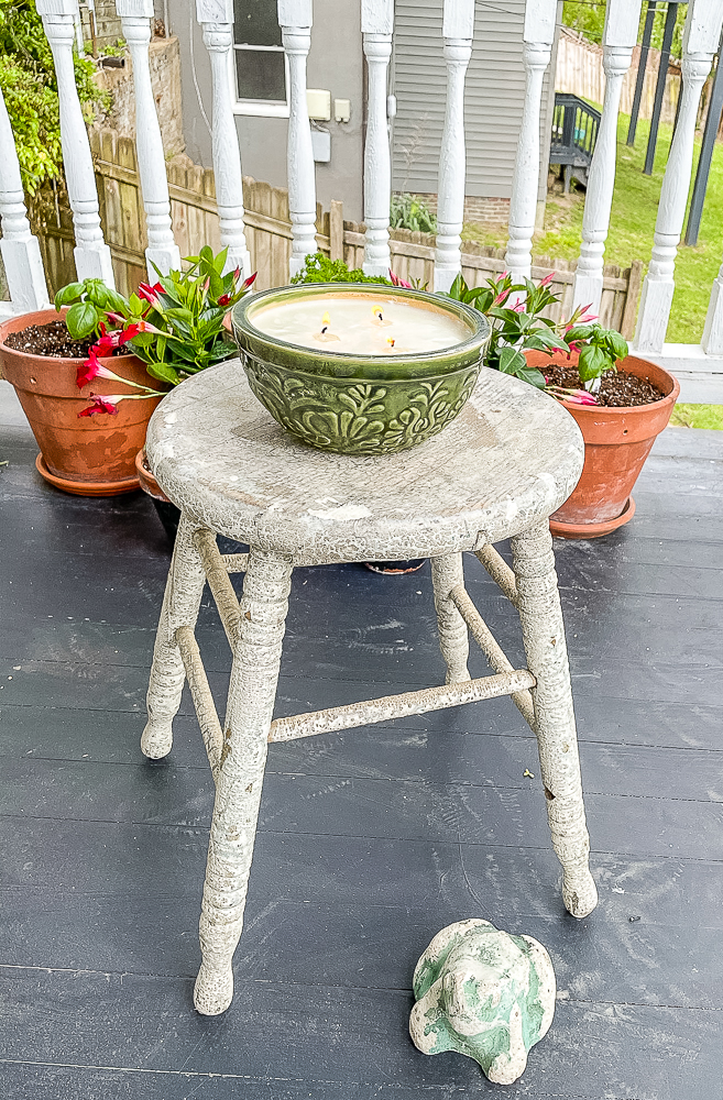 Homemade Citronella candle on an antique stool with potted flowers in the background