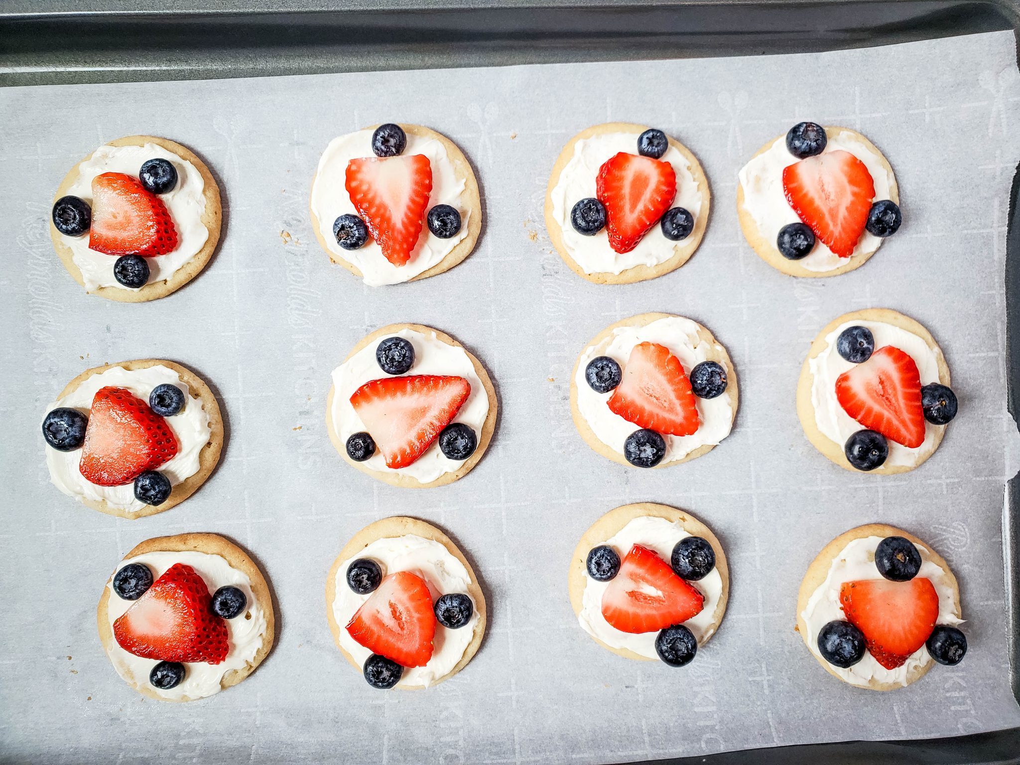 Sugar Cookies Iced with Cream Cheese Frosting and topped with a Strawberry slice and 3 Blueberries