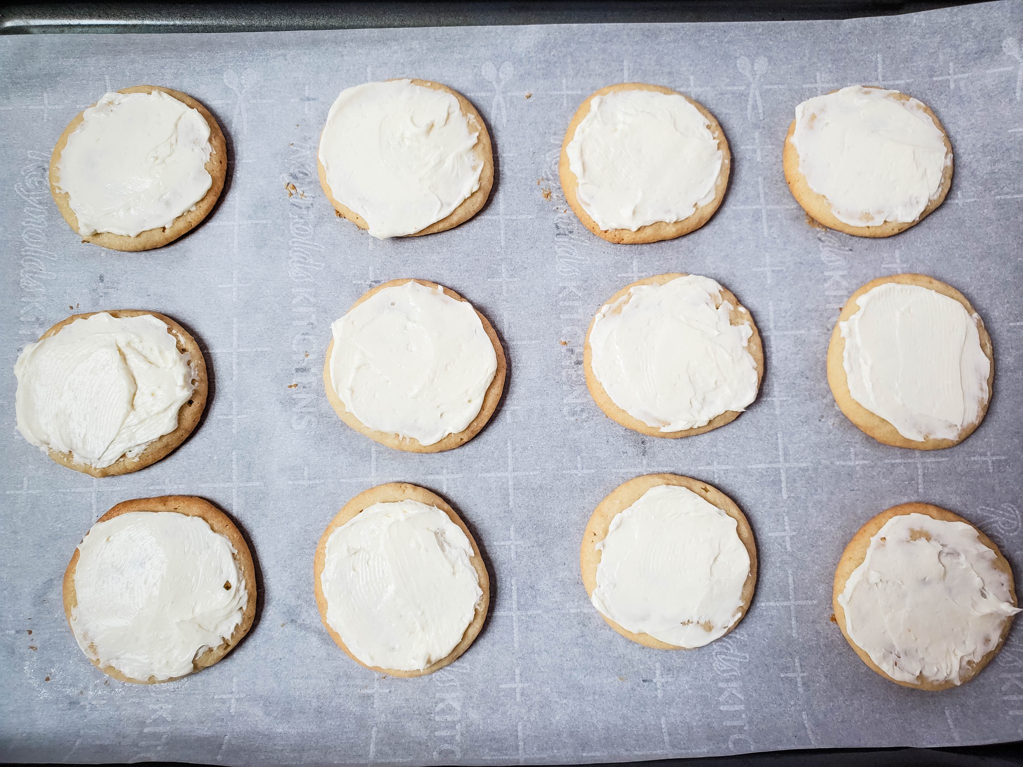 Sugar Cookies Iced with Cream Cheese Frosting on a Baking Sheet Lined with Parchment