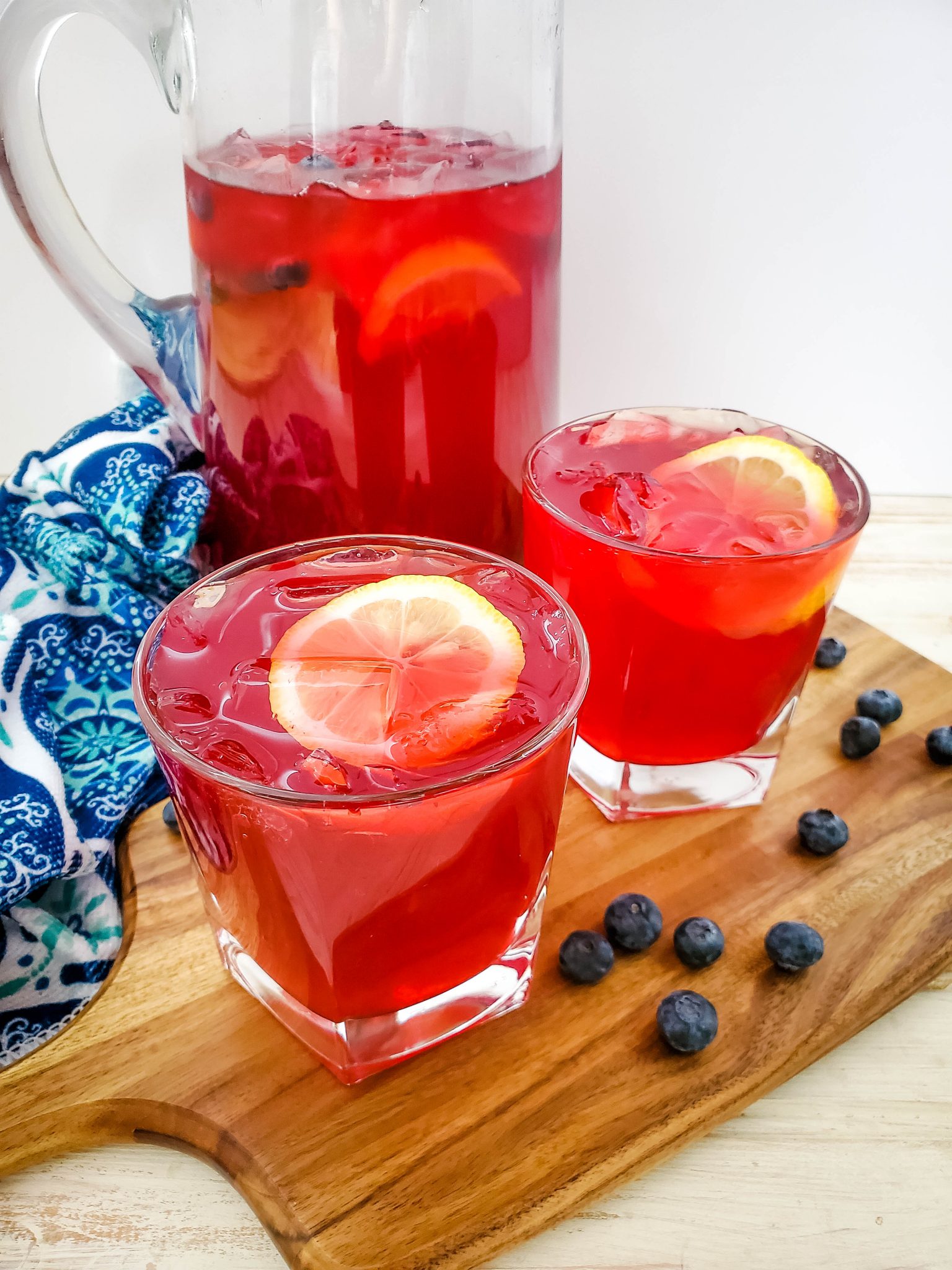 Homemade blueberry lemonade served in a pitcher with two poured glasses garnished with a lemon slice and blueberries