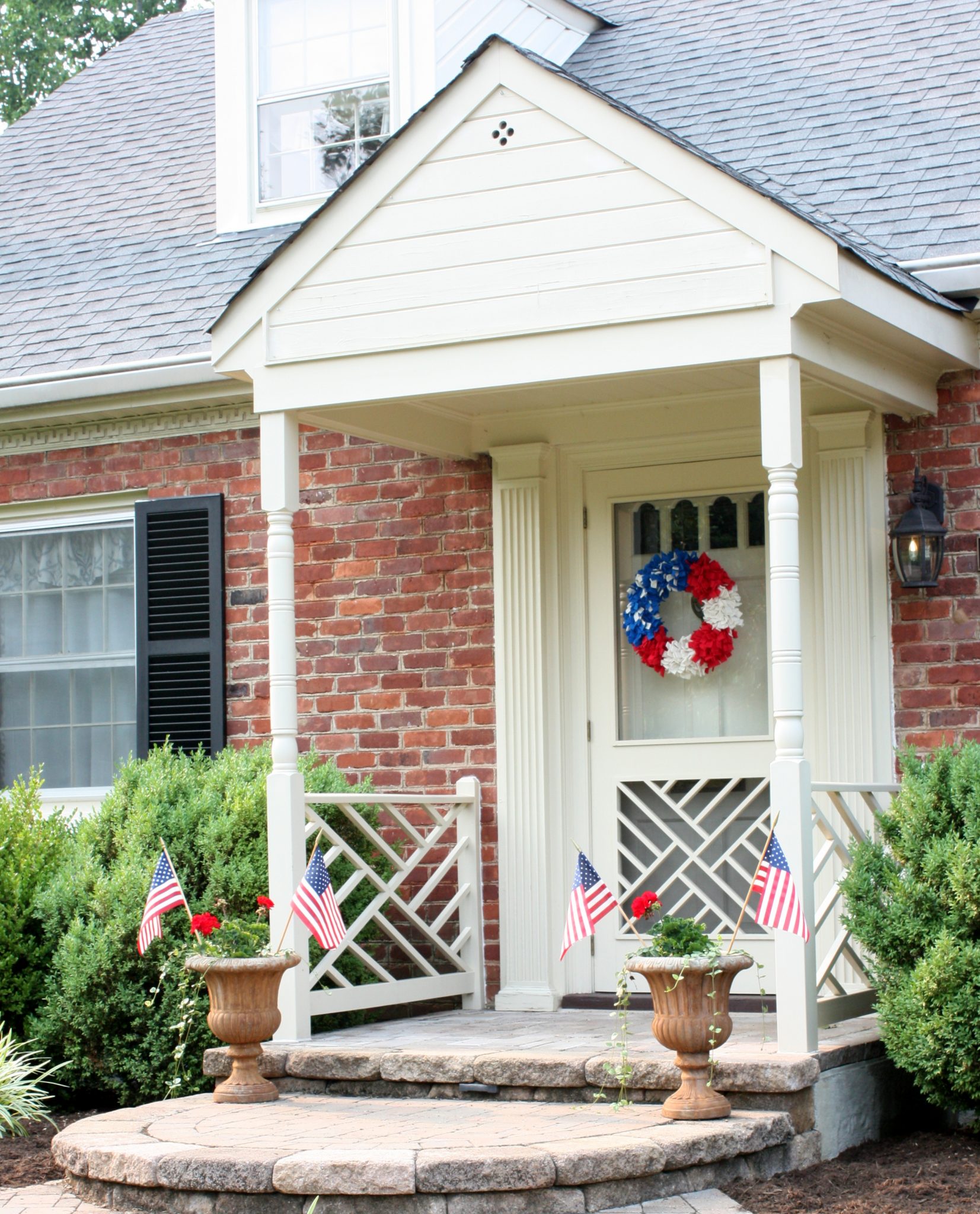 Front porch decorated with a red, white, and blue wreath and flags in flower pots.