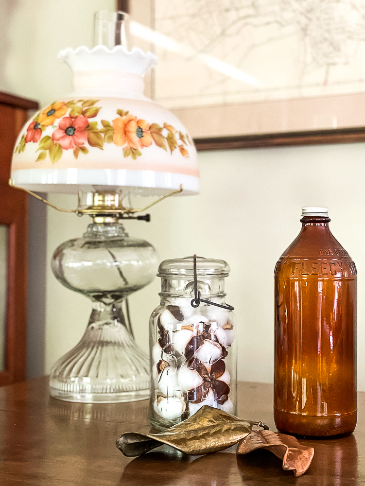 Antique oil lamp, vintage Mason jar filled with cotton bolls, Fleecy White amber bottle, and two preserved Magnolia leaves